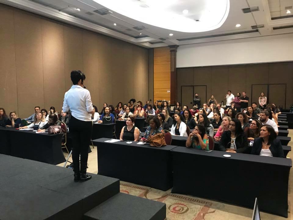 Patrícia Carvalho em palco palestrando para uma plateia de profissionais